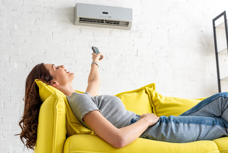 Women on yellow sofa pressing remote control to air conditioning unit