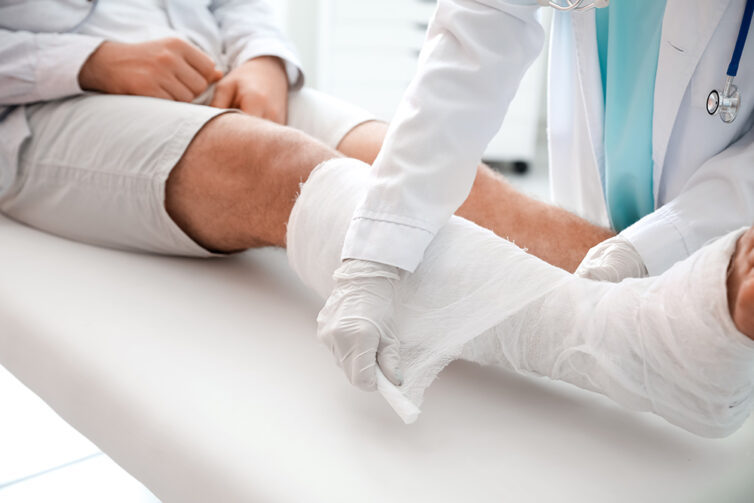 Doctor putting plaster cast on male patients right leg