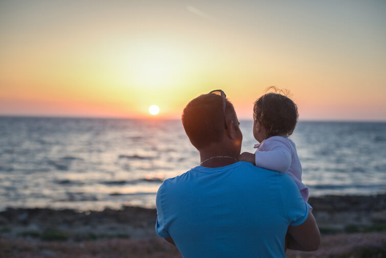 Man and baby at beach watching sunset