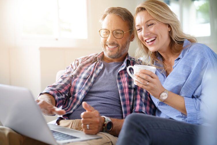 Couple sat on sofa and smiling, looking at laptop