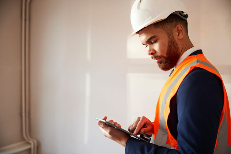 Chartered Surveyor checking property, wearing blue suit, visibility jacket and hard hat.