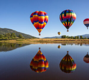 Multicoloured hot air balloons over lake in the countryside