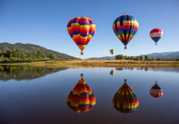 Multicoloured hot air balloons over lake in the countryside