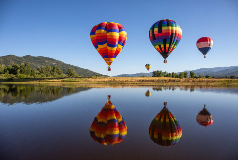 Multicoloured hot air balloons over lake in the countryside