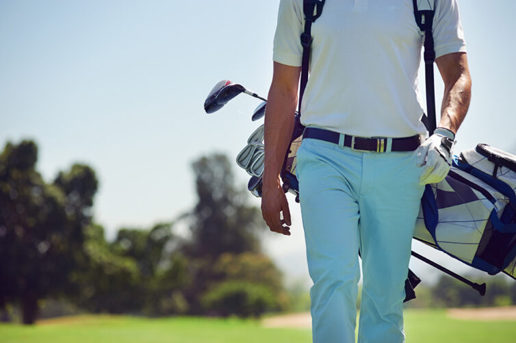 Golfer with blue trousers and white top, carrying golf bag