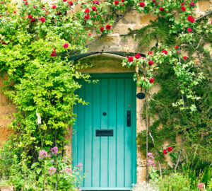 English stone cottage with roses climbing around green wooden door.