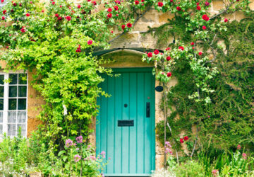 English stone cottage with roses climbing around green wooden door.