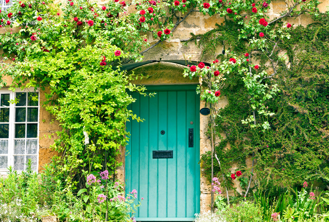 English stone cottage with roses climbing around green wooden door.