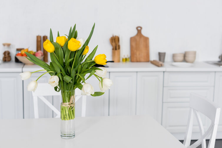 Vase of yellow and white tulips placed on table in white kitchen