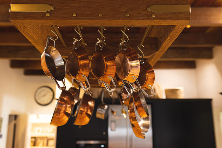 Copper kitchen pots and pans hanging from wooden rack over kitchen island