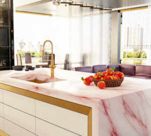 Modern designer kitchen with pink marble island counter top, with metal/brass draw triming and brass taps