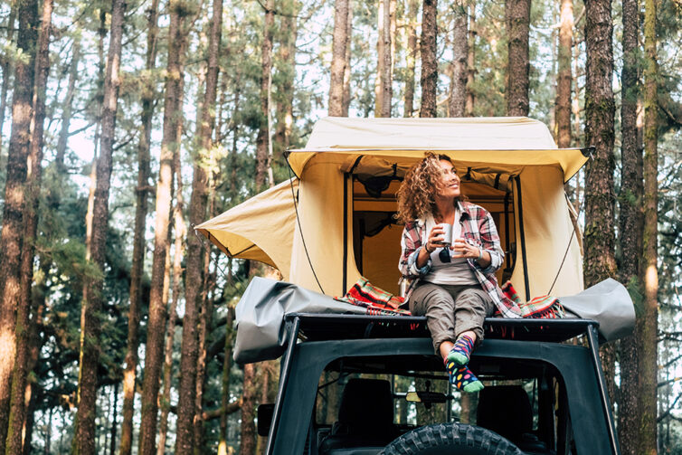 Women sat on car with tent on roof, parked in woodland