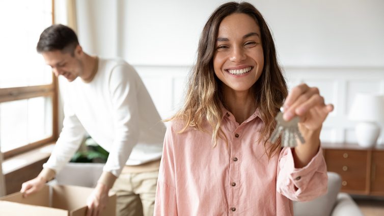 Male and female moving into new property. Women holding keys, man opening boxes