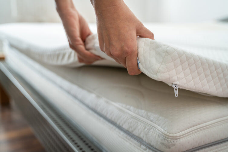 Matress topped being placed on bed with persons hands