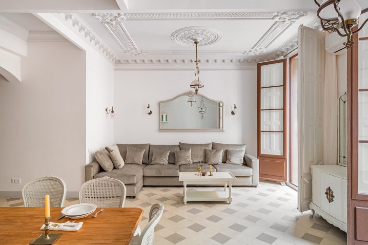 Classic living room with ceiling coving. Furniture including dining table and big sofa. Tiled flooring and large wooden double door.