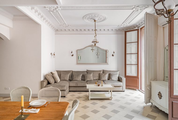 Classic living room with ceiling coving. Furniture including dining table and big sofa. Tiled flooring and large wooden double door.