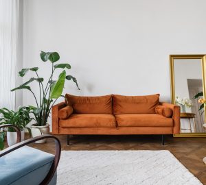 Retro looking sofa in orangy brown. Large plant wooden floors and large white rug