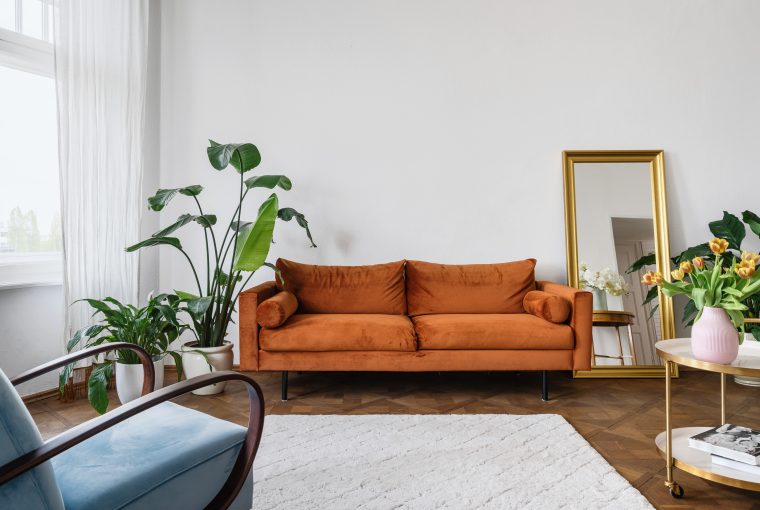 Retro looking sofa in orangy brown. Large plant wooden floors and large white rug