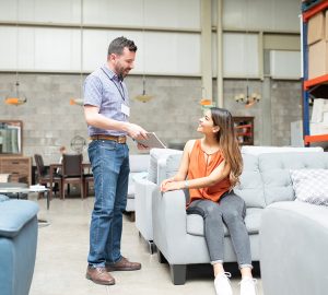 Women sitting on a grey sofa in a furniture store and talking to male shop assistant