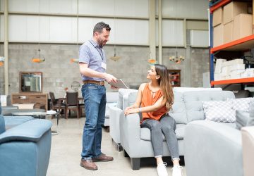 Women sitting on a grey sofa in a furniture store and talking to male shop assistant