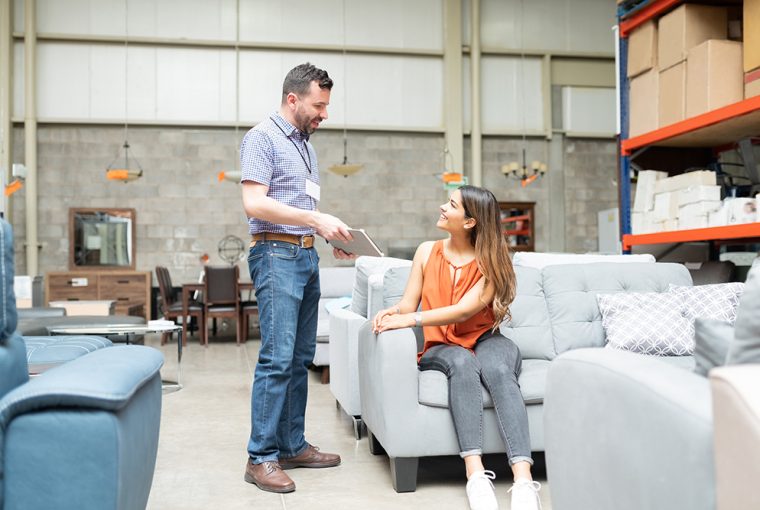 Women sitting on a grey sofa in a furniture store and talking to male shop assistant