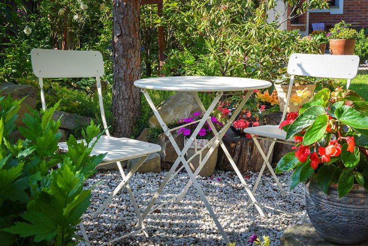 Metal garden bistro table and chairs placed on gravel in  the garden