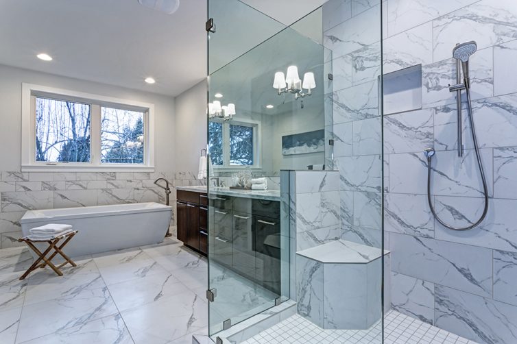 Modern white and marble bathroom with walk in shower, bath and dark coloured sink cabinet. Marble tile flooring, marble tile walls and marble tile sink surround