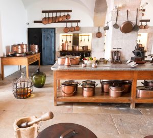 Old fashined kitchen with wooden island, hanging copper pots and natural tiled floors