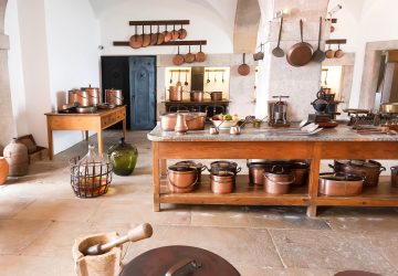 Old fashined kitchen with wooden island, hanging copper pots and natural tiled floors