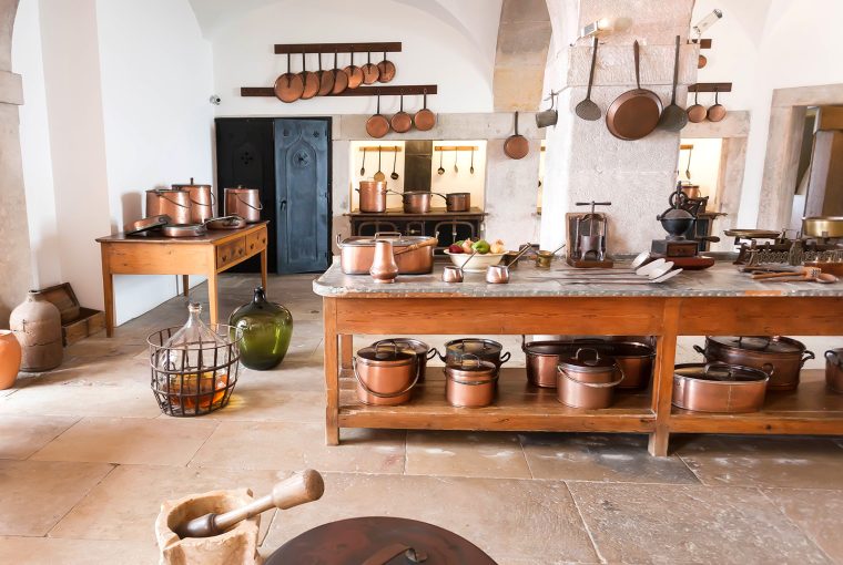 Old fashined kitchen with wooden island, hanging copper pots and natural tiled floors