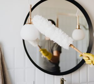 Dusting the large black round framed bathroom mirror