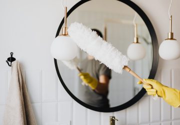 Dusting the large black round framed bathroom mirror