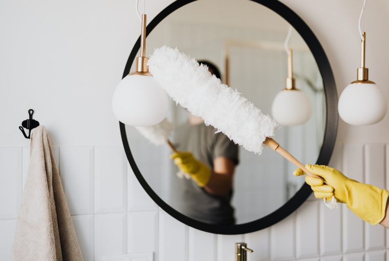 Dusting the large black round framed bathroom mirror